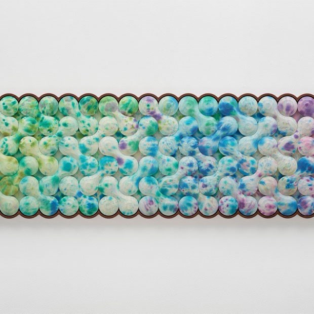 Abstract artwork featuring a horizontal grid of interconnected, rounded shapes in a gradient of pastel hues from green to blue and purple, framed with a scalloped brown border