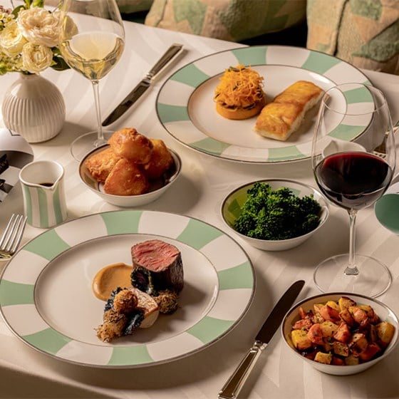 A refined dining table setting with a selection of gourmet dishes including tender beef fillet, seasonal vegetables, and rich sauces, complemented by red and white wine.