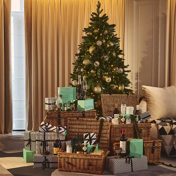 A decorated Christmas tree surrounded by wicker hampers, wrapped presents, and Claridge’s signature green gift boxes filled with festive food and wine.