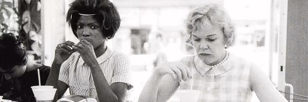 Photographs of two women in black and white, in 1950s dresses, in a coffee shop. The image is candid.