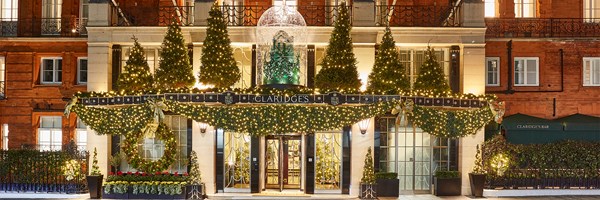 The façade of Claridge's adorned with festive decorations, including illuminated Christmas trees, garlands, and a sparkling glass dome centerpiece, against the backdrop of its iconic red-brick exterior.