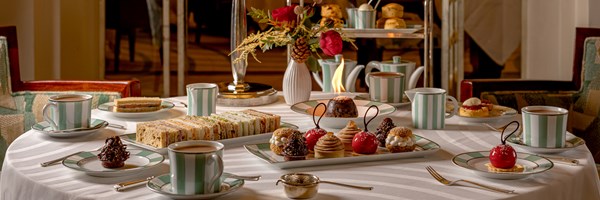 A refined afternoon tea setting with a classic table arrangement featuring delicate sandwiches, exquisite pastries, and freshly brewed tea in striped porcelain cups, accompanied by glasses of champagne, all illuminated by a soft lamp and surrounded by elegant decor.