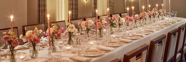 Claridge's pink and white flowers across a long table  laid with a white table cloth, crockery and pink candles