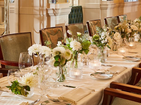 Tablescape featuring white table cloth,  crockery, and white flowers along the table arranged in small vases