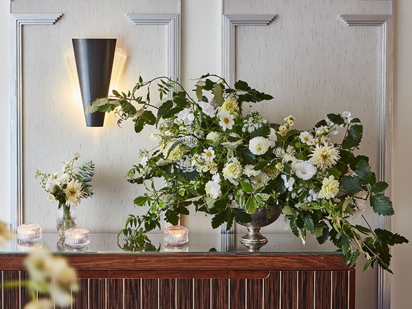 Beautiful and dramatic arrangement of a variety of white flowers in a metal vase, with a small vase on the left featuring a small display of white flowers.