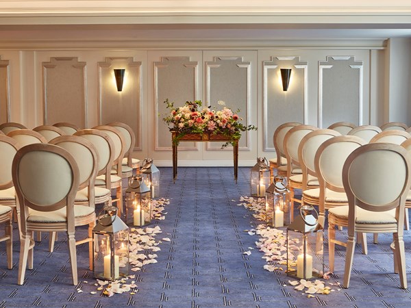 Event room laid out for a wedding with rows of chairs, petals up the aisle and big display of flowers at the top of the aisle