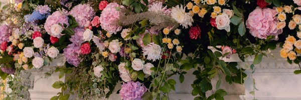 A luxurious floral arrangement featuring a cascading display of pink hydrangeas, roses, yellow spray roses, and soft greenery, set against a classic architectural backdrop.