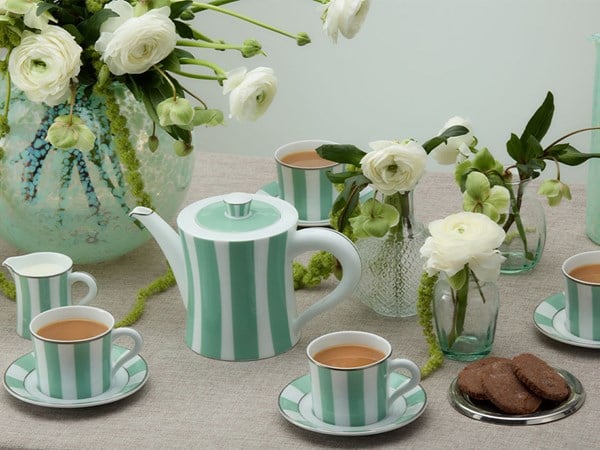 A beautifully arranged tea set featuring mint-green striped teacups, saucers, and a teapot, surrounded by white ranunculus flowers in glass vases, with chocolate biscuits on the side, exuding timeless elegance.