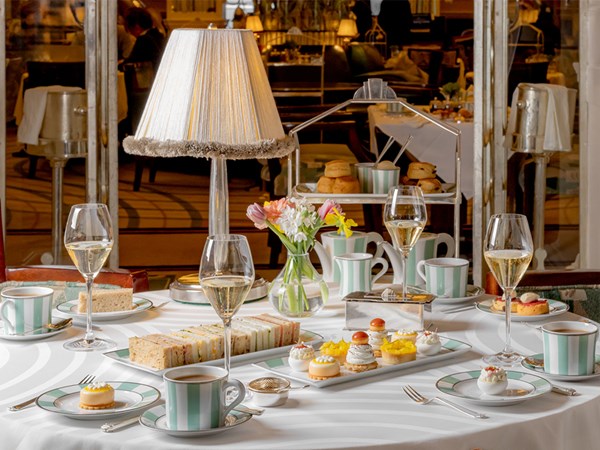 The Foyer and Reading Room afternoon tea set up with finger sandwiches and pastries set on the table, scones with jam and cream in the background and full glasses of champagne