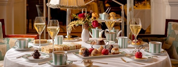 The first image showcases a refined afternoon tea spread with an assortment of elegant sandwiches and intricate pastries, paired with a glass of Champagne on Claridge’s signature green and white striped china.