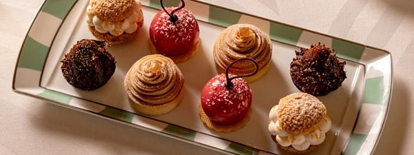 a platter of exquisitely crafted pastries, including a red fruit-glazed dessert, a Mont Blanc swirl, and golden-topped choux puffs, arranged with artistic precision.