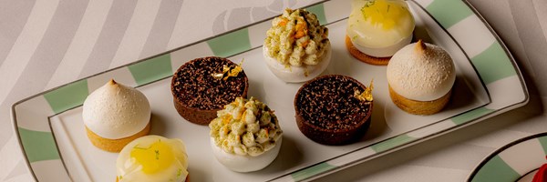 A selection of exquisite pastries and tarts, meticulously arranged on a signature green-and-white striped Claridge's plate, showcasing delicate meringues, rich chocolate tarts with gold leaf, and citrus-infused confections.