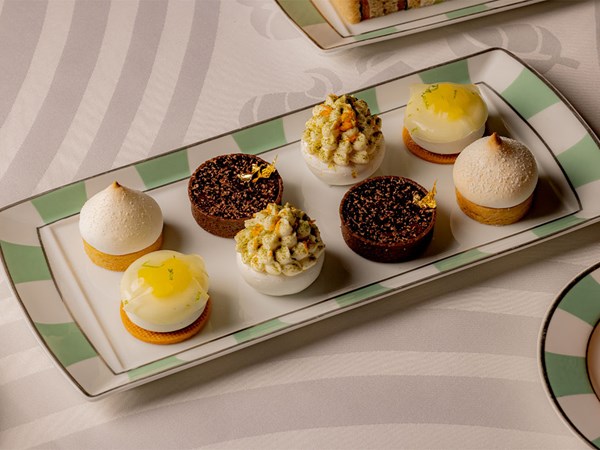 An exquisite platter of handcrafted desserts, including citrus-infused confections, chocolate delicacies, and piped meringue creations, artfully placed on Claridge’s signature green and white porcelain.