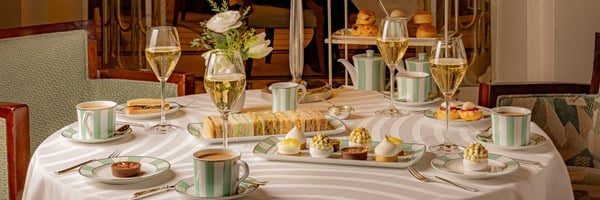 A beautifully set afternoon tea at Claridge’s, featuring an elegant spread of finger sandwiches, fine pastries, scones, and champagne, served on the iconic green-and-white striped china in a refined, light-filled setting.