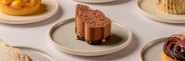 A meticulously crafted, chocolate mousse dessert adorned with delicate gold leaf, resting on a minimalist plate, exemplifying modern pâtisserie elegance.