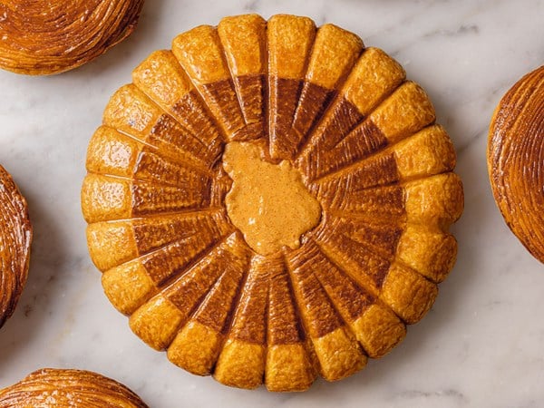 A top-down view of a beautifully arranged galette des rois, featuring a symmetrical, scalloped pattern with a glossy finish and a decorative center.