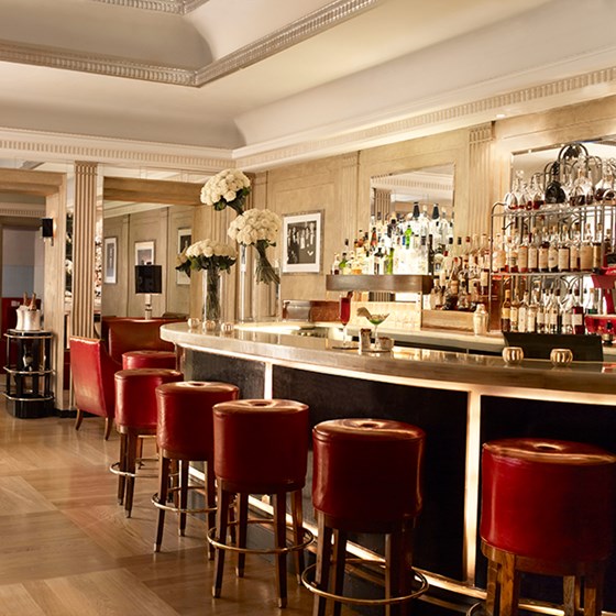 A view of red bar stools and a warm interior with floral arrangements at Claridge's Bar