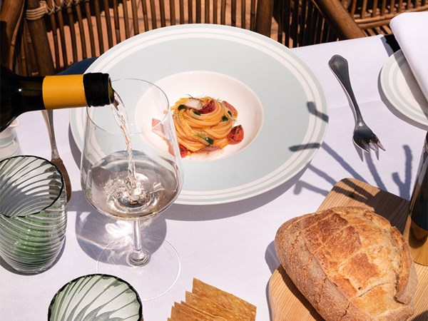 Al fresco dining: Wine pours into a glass beside a vibrant pasta dish, artisan bread, and elegant tableware