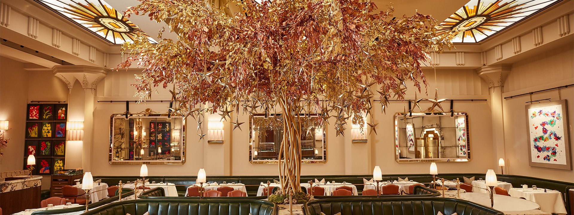 An opulent dining space featuring a central golden tree sculpture adorned with shimmering leaves and hanging stars, surrounded by green leather banquettes and elegant table settings under intricate skylights.