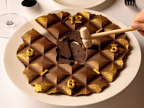 Elegant chocolate dessert shaped like a clock face with golden accents and numbers, being gently tapped with a small wooden hammer, inviting an interactive and luxurious dining experience