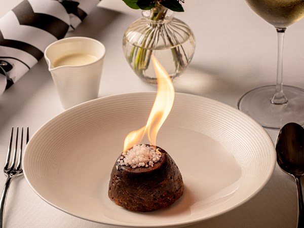 An elegant decorated festive table, with a christmas pudding up in flames.