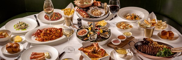 Decadent spread of delicious food on table, including oysters, spaghetti, prawns, steak, red wine and white wine.