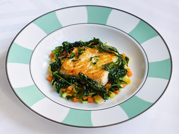 A beautifully plated fish dish, accompanied by sautéed greens and a vibrant vegetable medley.