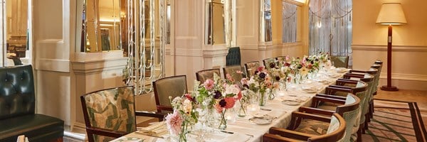 The Foyer Private Dining Room at Claridge's featuring a table with a white table cloth, crockery, pink flowers in vases and candles.