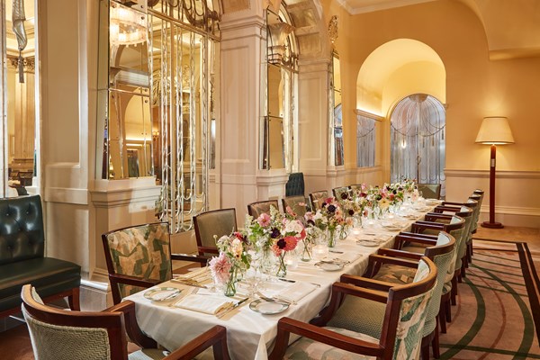 The Foyer Private Dining Room at Claridge's featuring a table with a white table cloth, crockery, pink flowers in vases and candles.