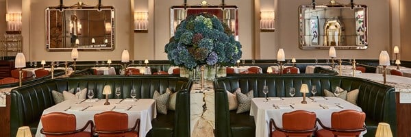 Claridge's restaurant with green banquets, set tables and a big vase of blue hydrangeas in the centre
