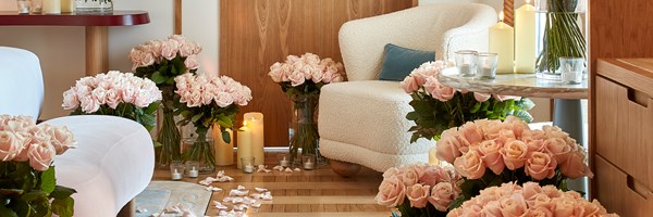 A wider view of the romantic hotel suite, where an abundance of pink roses, glowing candlelight, and plush furnishings set the stage for an unforgettable moment of love and elegance.