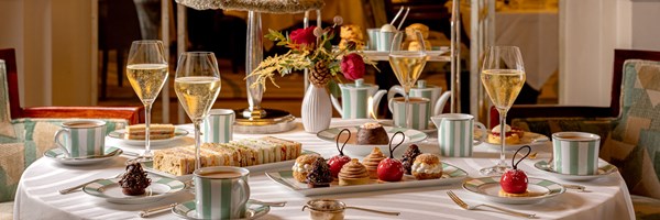 An elegant afternoon tea setting featuring champagne, fine china, sandwiches, and decadent pastries at Claridge's.