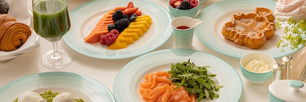 A vibrant breakfast spread with fresh fruits, pastries, smoked salmon, waffles, and a green smoothie on pastel tableware.