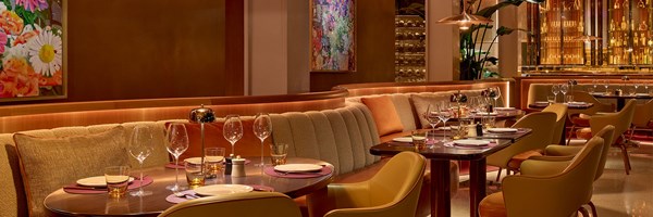 A warm, modern dining area with cushioned booths, polished tables, floral artwork, and golden accents, offering a luxurious dining experience.